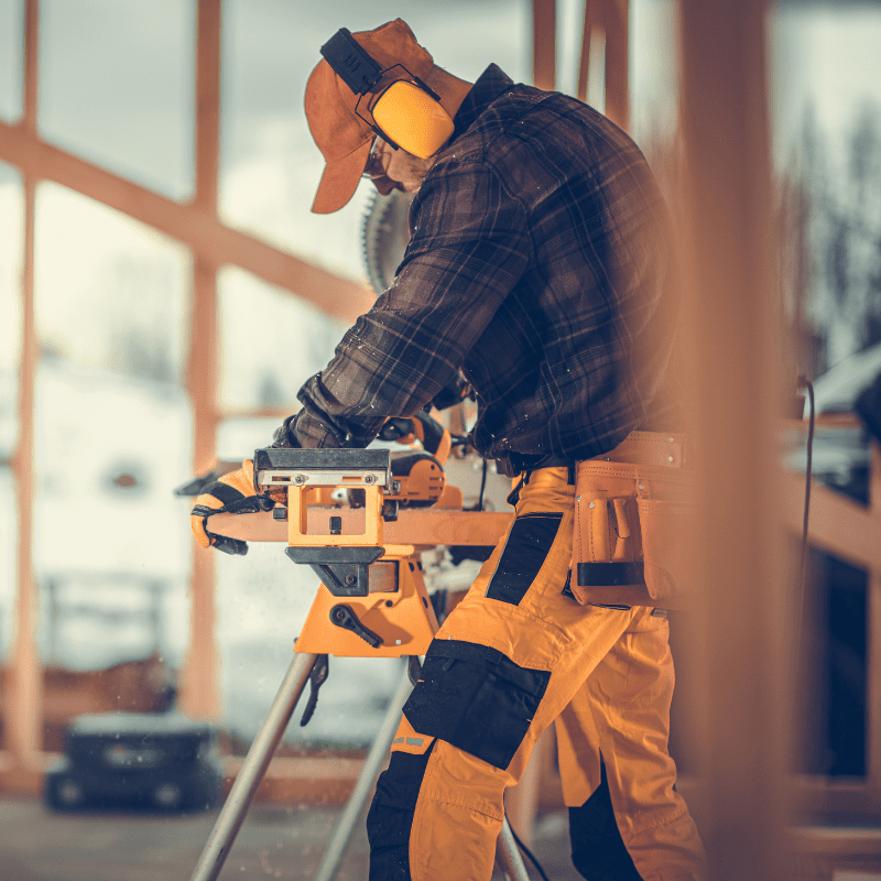 A crafts trades professional is learns how to become a carpenter as they are cutting wood on a sawhorse.