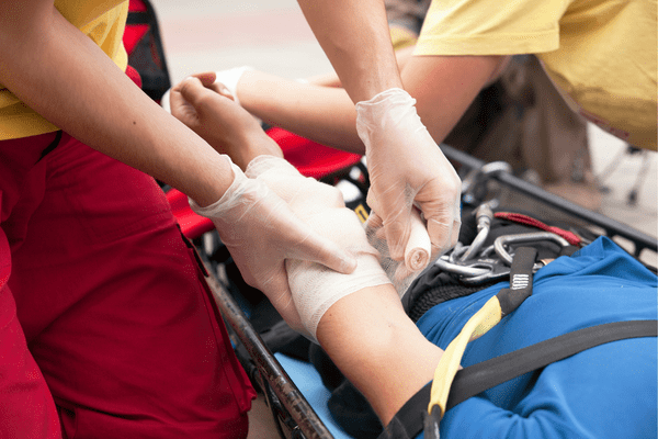A First Aid trained person applies a bandage to an injured person in a stretcher