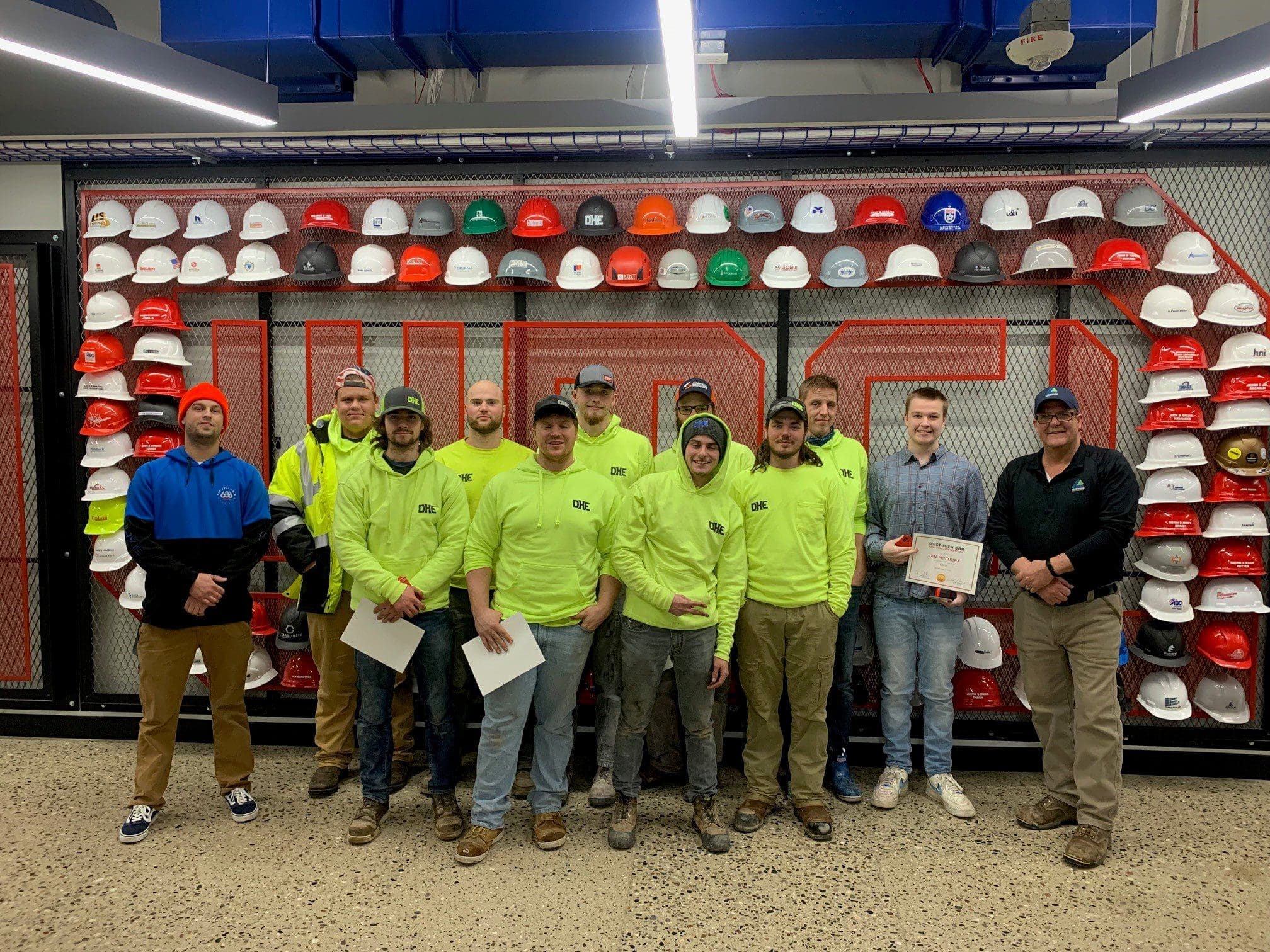 Group of Carpentry I graduates stand in front of the WMCI hard hat wall with their instructor - Clark Causely