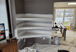 The second step in drywalling instructor Clark Causely's home project creating an alcove for his living room. The three shelves have been drywalled and are now flush with the triangular wall they are housed in.