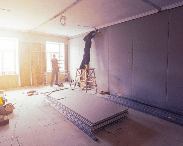 Two drywall installers finishing a wall in a commercial construction project.