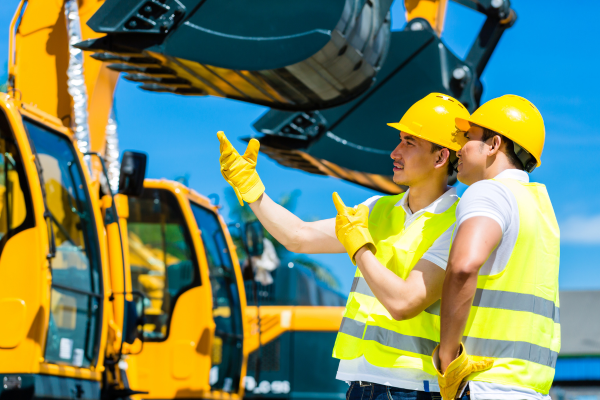 Two construction workers from different backgrounds communicate with each other on a job site.
